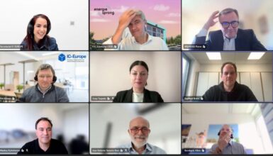 Nine-person video conference grid with nine tiles, each person visible in their own frame, some with company logos or branded backgrounds.