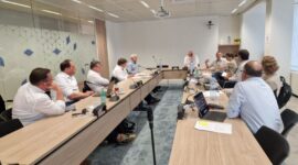 Team of professionals seated around a U-shaped conference table in a modern meeting room, discussing documents.