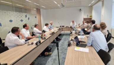 Team of professionals seated around a U-shaped conference table in a modern meeting room, discussing documents.