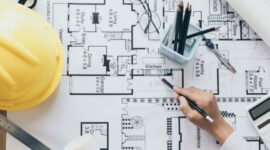 Architectural floor plan being studied with drafting tools and a yellow construction helmet nearby.