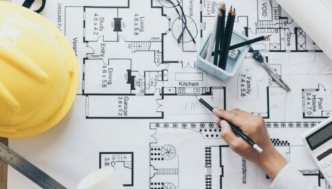 Architectural floor plan being studied with drafting tools and a yellow construction helmet nearby.