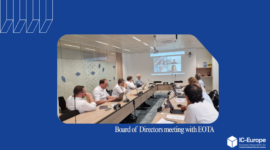Board of Directors meeting in a conference room with people seated around a long table and a video conference on the wall screen (IC-Europe branding).