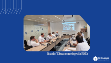 Board of Directors meeting in a conference room with people seated around a long table and a video conference on the wall screen (IC-Europe branding).